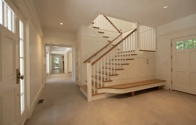 Bright entryway with a white staircase and built-in storage under the steps, a curved bench, and a front door with glass panels.