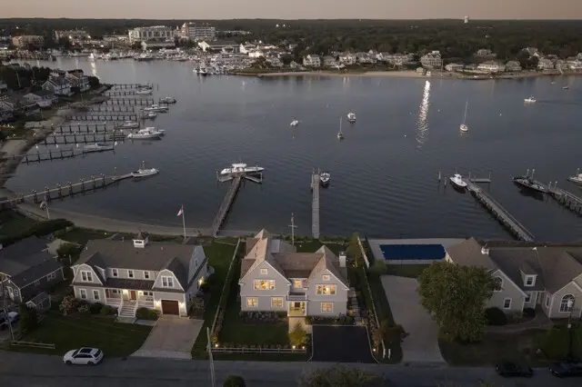 Aerial view of a coastal town with boats at docks, marinas, and waterfront homes along a calm harbor at dusk.