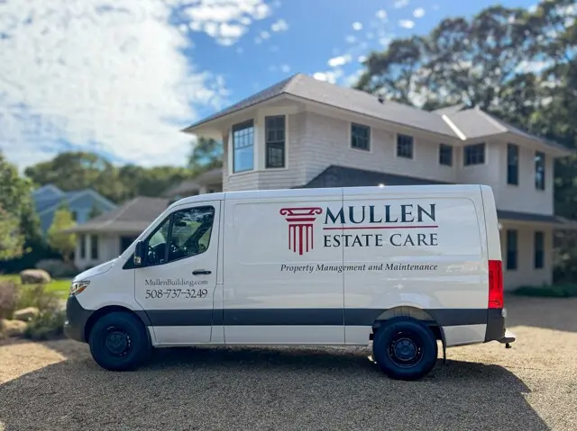 White van with Mullen Estate Care branding on its side parked in front of a two-story beige house on a sunny day.