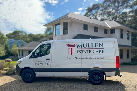 White van with Mullen Estate Care branding on its side parked in front of a two-story beige house on a sunny day.